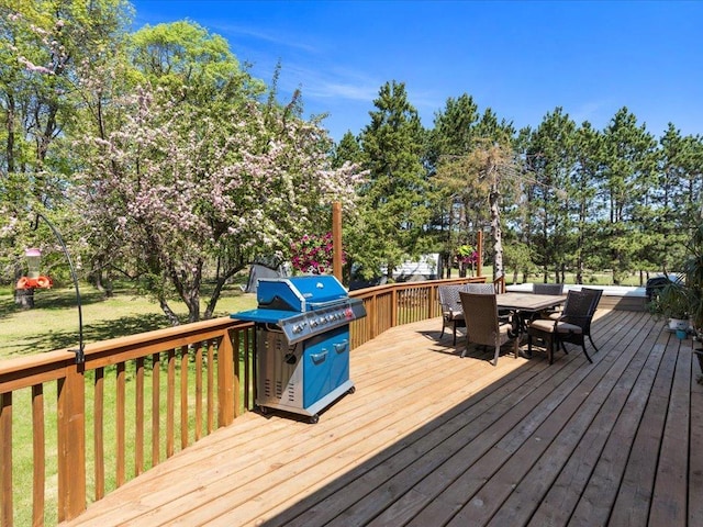wooden terrace with area for grilling, outdoor dining space, view of scattered trees, and a lawn