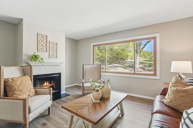 living room with a fireplace with flush hearth, light wood-type flooring, a textured ceiling, and baseboards