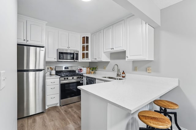 kitchen featuring appliances with stainless steel finishes, a sink, a peninsula, a breakfast bar, and light wood-type flooring