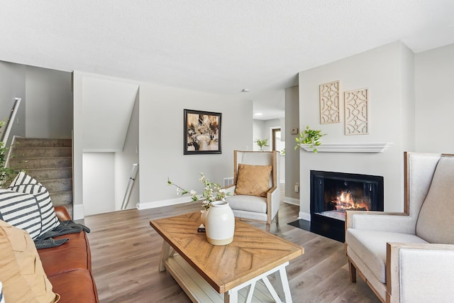 living room featuring wood finished floors, a fireplace with flush hearth, baseboards, and stairs