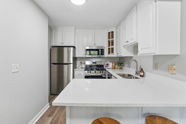 kitchen with stainless steel appliances, a sink, light wood-style floors, a peninsula, and a kitchen bar