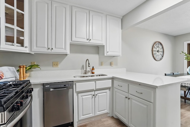 kitchen with stainless steel appliances, a sink, light wood finished floors, and white cabinets