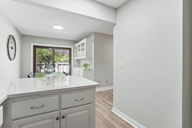 kitchen featuring baseboards, light wood-style flooring, white cabinetry, glass insert cabinets, and light stone counters