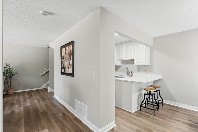 kitchen featuring a breakfast bar area, light wood-style floors, white cabinetry, light countertops, and a textured ceiling