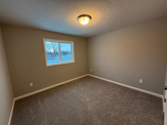 empty room with dark colored carpet, baseboards, and a textured ceiling