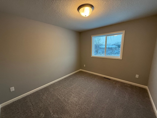 spare room with a textured ceiling, dark carpet, and baseboards