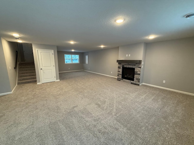 below grade area featuring baseboards, stairway, carpet flooring, a stone fireplace, and a textured ceiling