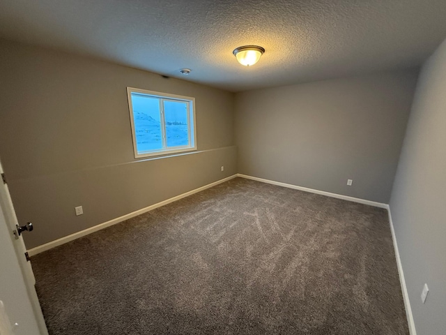 spare room featuring a textured ceiling, dark carpet, and baseboards