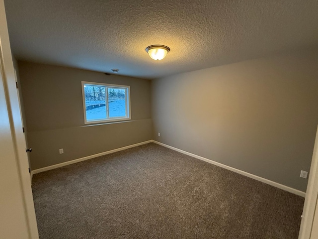 spare room featuring dark colored carpet, a textured ceiling, and baseboards