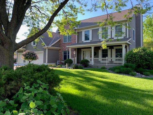 view of front of house featuring covered porch, a front yard, a chimney, and a garage