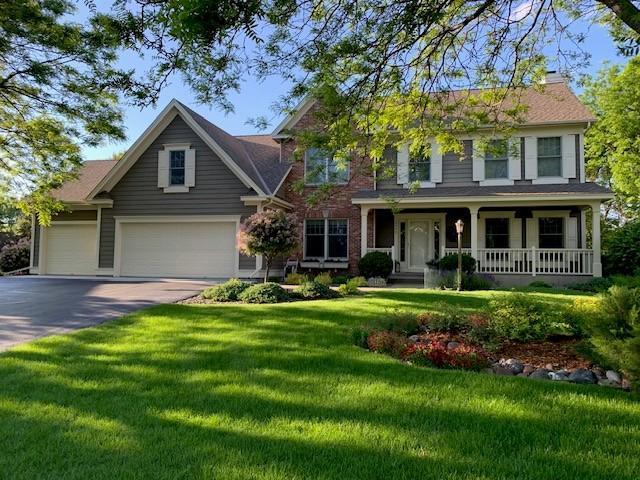 view of front of property featuring covered porch, an attached garage, asphalt driveway, a front yard, and a chimney