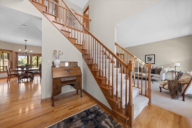 stairs featuring wood finished floors, a chandelier, a high ceiling, and baseboards