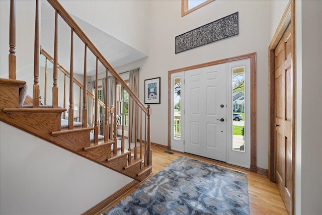 entrance foyer with wood finished floors, stairway, baseboards, and a high ceiling