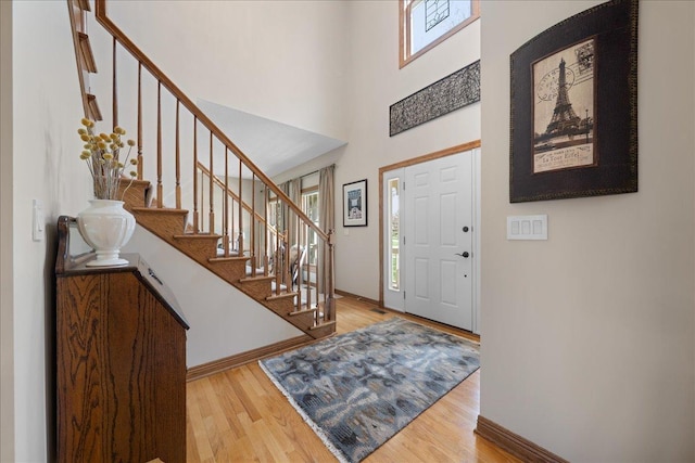 foyer with wood finished floors, stairs, baseboards, and a towering ceiling