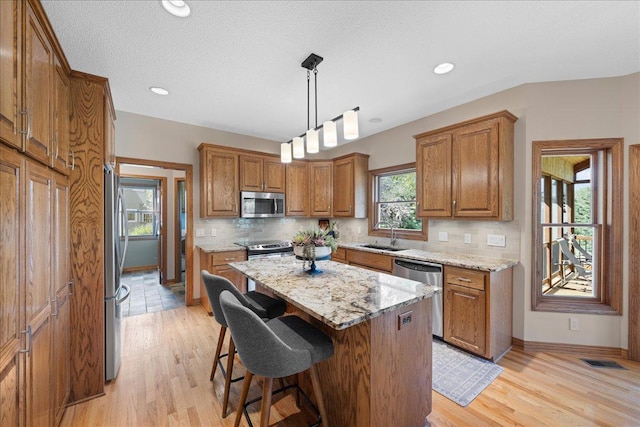 kitchen with appliances with stainless steel finishes, brown cabinets, tasteful backsplash, a kitchen island, and recessed lighting