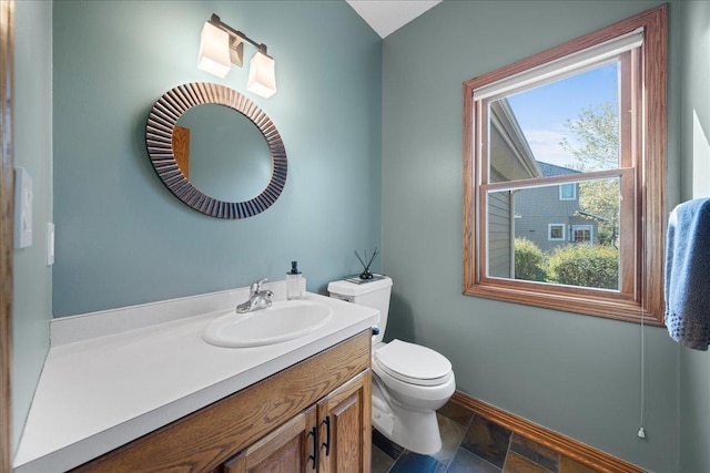 bathroom with toilet, vanity, baseboards, and stone finish floors