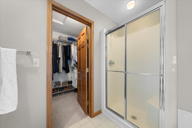 full bath featuring a textured ceiling, a stall shower, a walk in closet, and tile patterned floors