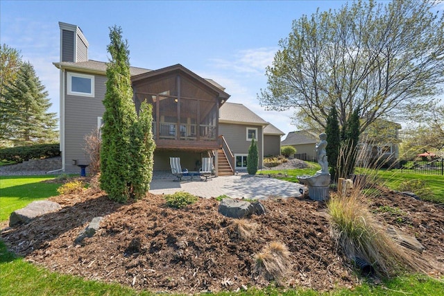 rear view of property featuring a patio, a sunroom, a chimney, and stairway