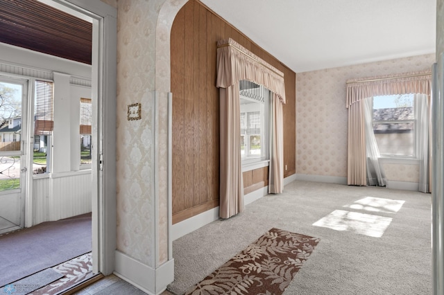 empty room with carpet, wallpapered walls, and arched walkways