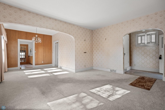 unfurnished room featuring arched walkways, a chandelier, plenty of natural light, and carpet flooring