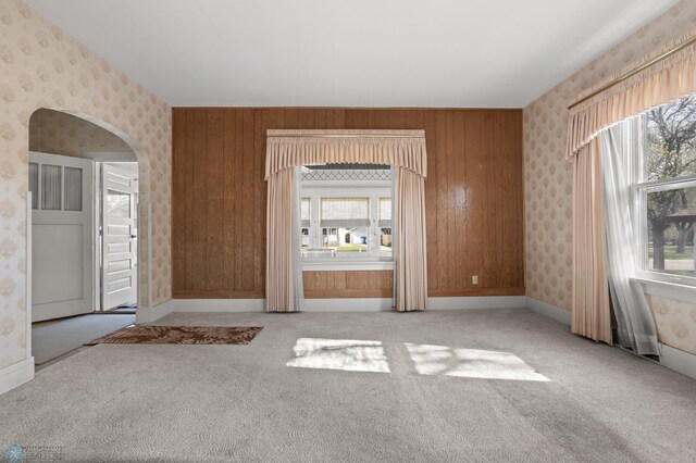 unfurnished room featuring wallpapered walls, plenty of natural light, carpet floors, arched walkways, and baseboards
