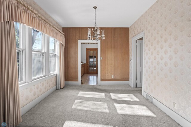 unfurnished room featuring a chandelier, light carpet, wallpapered walls, and wooden walls