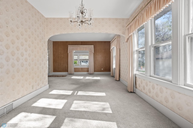 spare room featuring arched walkways, wallpapered walls, a chandelier, and light carpet