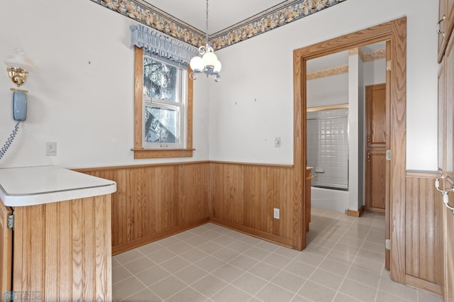 unfurnished dining area with wainscoting, healthy amount of natural light, light tile patterned flooring, and wooden walls