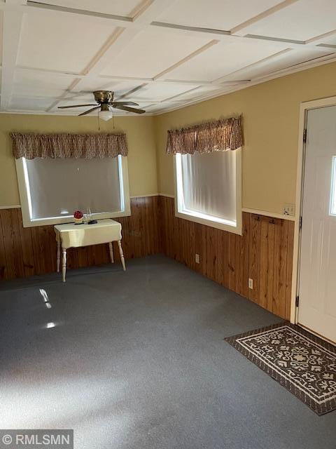 entryway featuring wainscoting, wood walls, a ceiling fan, and carpet