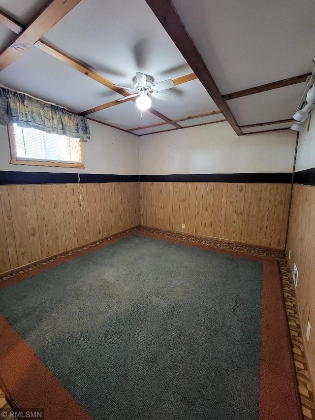 carpeted empty room with wood walls, ceiling fan, baseboards, and wainscoting