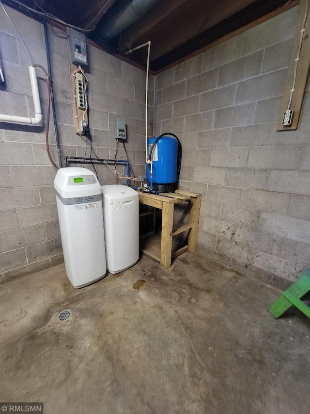 unfinished below grade area featuring concrete block wall, a water softener system, and a water pressure tank