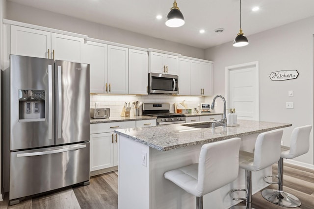 6813 5th St N, Brooklyn Center, MN 55430 - kitchen with appliances with stainless steel finishes, a sink, light wood-style floors, an island with sink, and backsplash