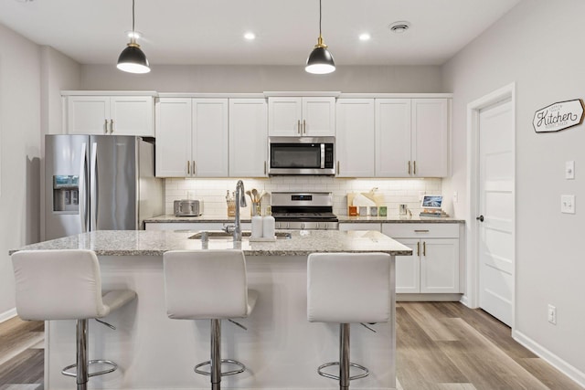 6813 5th St N, Brooklyn Center, MN 55430 - kitchen featuring appliances with stainless steel finishes, light wood-style floors, a sink, an island with sink, and backsplash
