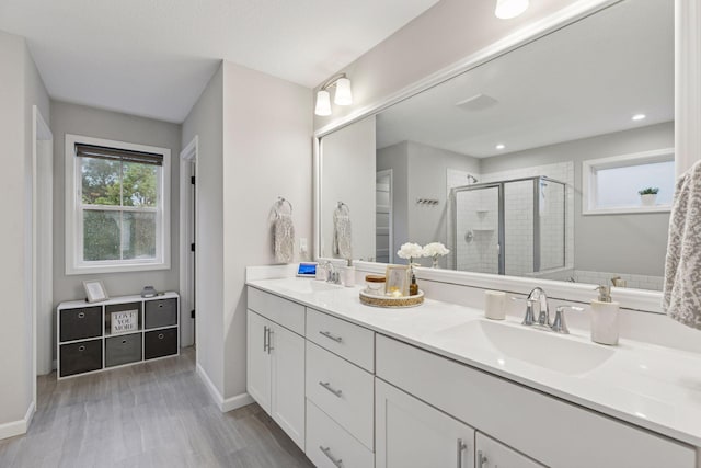 6813 5th St N, Brooklyn Center, MN 55430 - bathroom with a stall shower, double vanity, wood finished floors, and baseboards