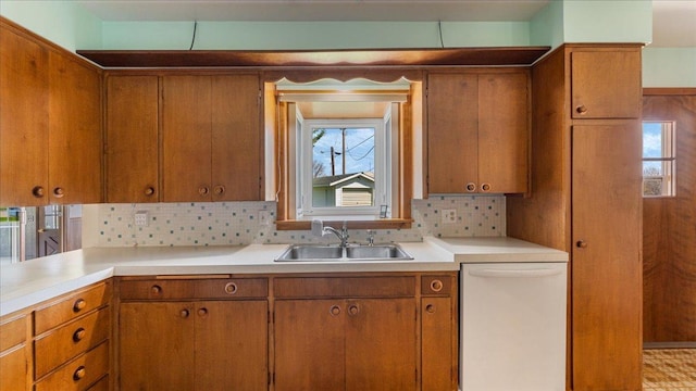 kitchen with white dishwasher, a sink, brown cabinets, and light countertops