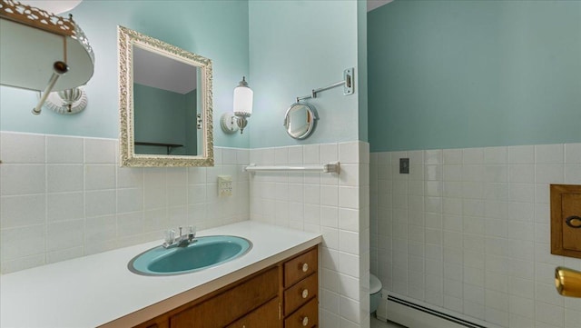 bathroom featuring a baseboard heating unit, tile walls, toilet, vanity, and wainscoting