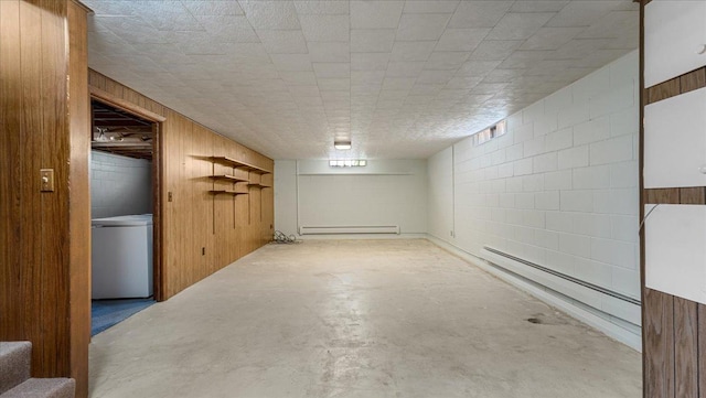 finished basement featuring concrete block wall, baseboard heating, wooden walls, fridge, and washer / clothes dryer