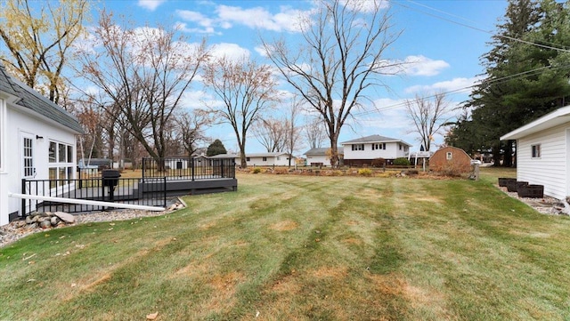 view of green lawn featuring a wooden deck, an outdoor structure, and a storage unit