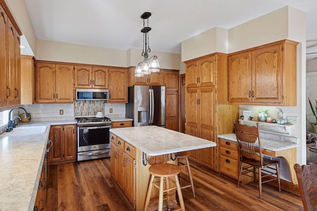 kitchen with stainless steel appliances, a sink, brown cabinetry, light countertops, and dark wood finished floors