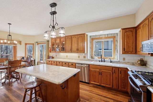 kitchen with appliances with stainless steel finishes, a sink, a chandelier, a textured ceiling, and wood finished floors