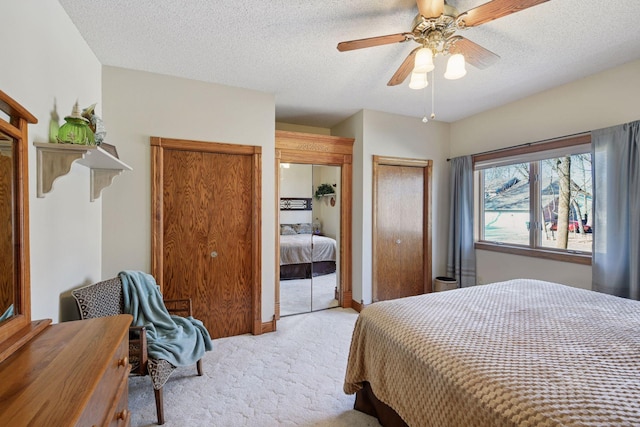 bedroom with light carpet, multiple closets, a textured ceiling, and a ceiling fan