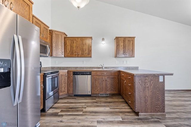 kitchen featuring stainless steel appliances, a peninsula, dark wood-style floors, high vaulted ceiling, and brown cabinets