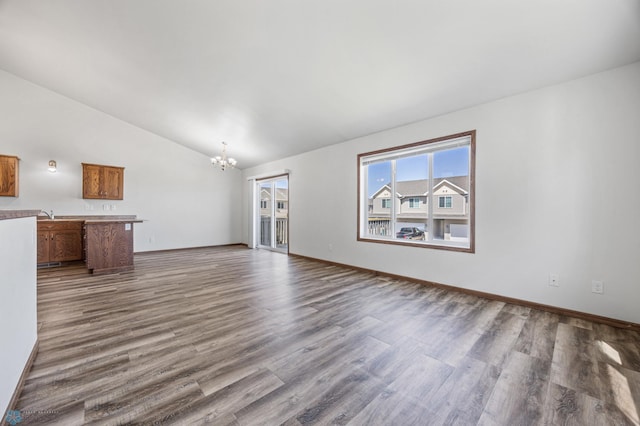 unfurnished living room with a chandelier, lofted ceiling, dark wood-type flooring, and baseboards