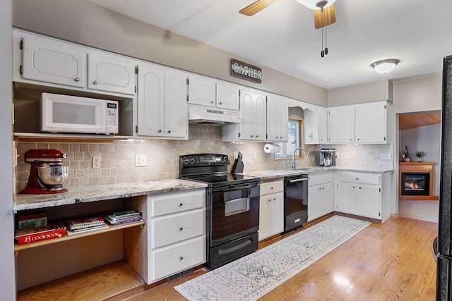 kitchen with black appliances, under cabinet range hood, white cabinetry, tasteful backsplash, and light wood-style floors