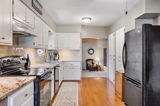 kitchen with black appliances, under cabinet range hood, white cabinetry, light wood finished floors, and backsplash