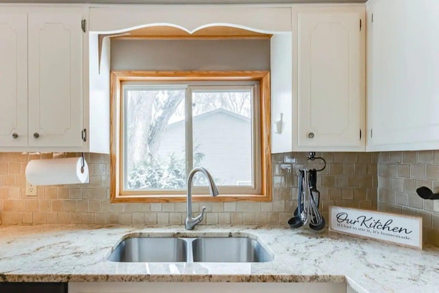 kitchen view of a sink, white cabinets, tasteful backsplash, and light stone countertops