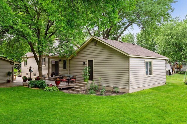 rear view of house featuring a yard, a wooden deck, and a shingled roof