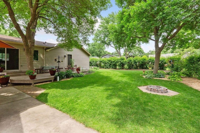 view of grassy yard with a deck and an outdoor fire pit