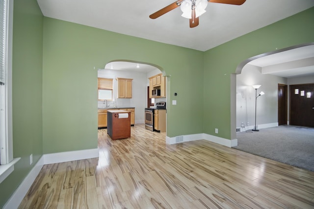 733 1st St SW, Faribault, MN 55021 - unfurnished living room featuring ceiling fan, arched walkways, light wood-type flooring, baseboards, and a sink
