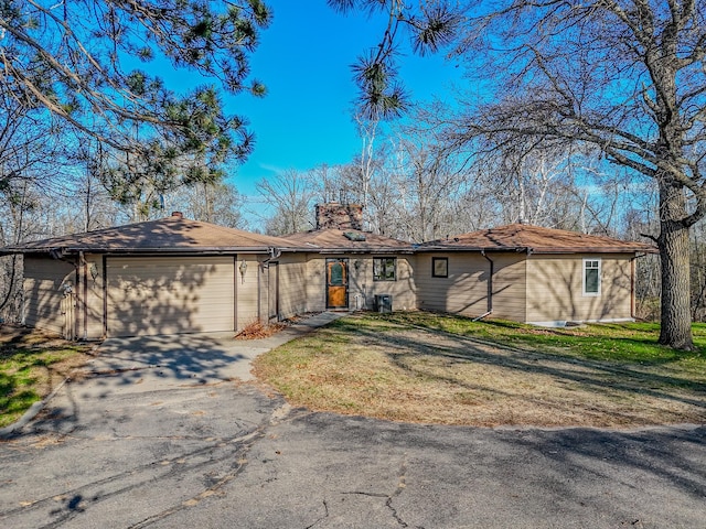 ranch-style home featuring an attached garage, asphalt driveway, a chimney, and a front lawn